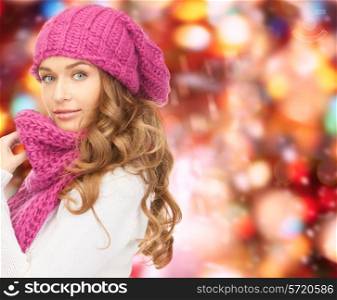 happiness, winter holidays, christmas and people concept - young woman in pink hat and scarf over red lights background