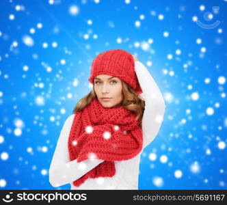 happiness, winter holidays, christmas and people concept - young woman in red hat and scarf over blue snowy background