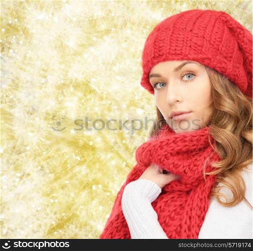 happiness, winter holidays, christmas and people concept - young woman in red hat and scarf over yellow lights background
