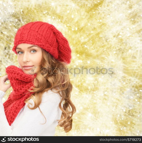 happiness, winter holidays, christmas and people concept - young woman in red hat and scarf over yellow lights background