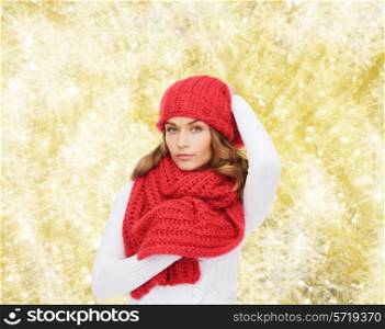 happiness, winter holidays, christmas and people concept - young woman in red hat and scarf over yellow lights background