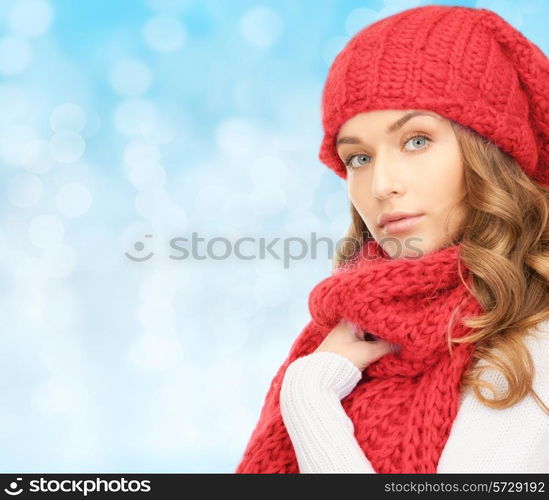 happiness, winter holidays, christmas and people concept - young woman in red hat and scarf over blue lights background