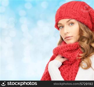 happiness, winter holidays, christmas and people concept - young woman in red hat and scarf over blue lights background