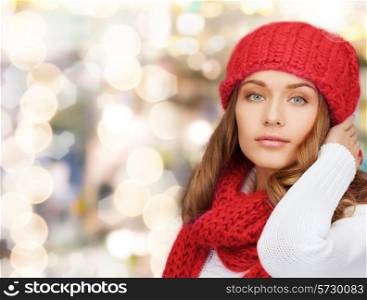 happiness, winter holidays, christmas and people concept - young woman in red hat and scarf over lights background