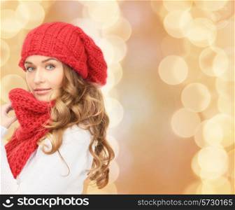 happiness, winter holidays, christmas and people concept - young woman in red hat and scarf over beige lights background