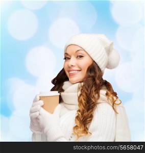 happiness, winter holidays, christmas, beverages and people concept - smiling young woman in white hat and mittens with coffee cup over blue lights background