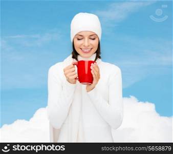happiness, winter holidays, christmas, beverages and people concept - smiling young woman in white warm clothes with red cup over blue sky and white cloud background