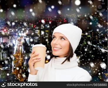 happiness, winter holidays, christmas, beverages and people concept - smiling young woman in white hat and mittens with coffee cup over snowy night city background
