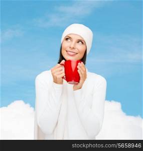 happiness, winter holidays, christmas, beverages and people concept - smiling young woman in white warm clothes with red cup over blue sky and white cloud background