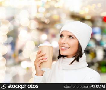 happiness, winter holidays, christmas, beverages and people concept - smiling young woman in white hat and mittens with coffee cup over lights background