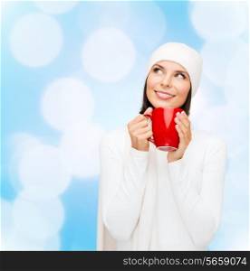 happiness, winter holidays, christmas, beverages and people concept - smiling young woman in white warm clothes with red cup over blue lights background