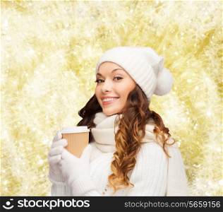 happiness, winter holidays, christmas, beverages and people concept - smiling young woman in white hat and mittens with coffee cup over yellow lights background