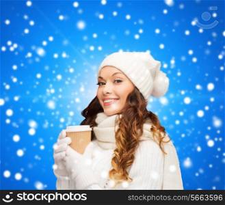 happiness, winter holidays, christmas, beverages and people concept - smiling young woman in white hat and mittens with coffee cup over blue snowy background