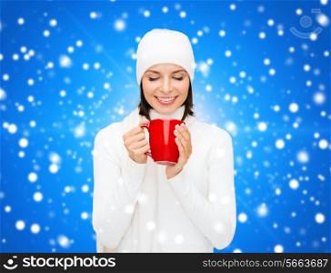 happiness, winter holidays, christmas, beverages and people concept - smiling young woman in white warm clothes with red cup over blue snowy background
