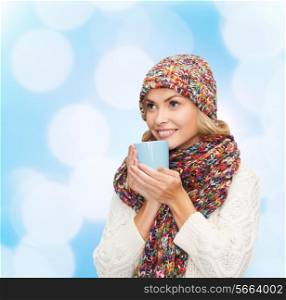 happiness, winter holidays, christmas, beverages and people concept - smiling young woman in warm clothes with cup over blue lights background