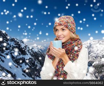 happiness, winter holidays, christmas, beverages and people concept - smiling young woman in warm clothes with cup over snowy mountains background