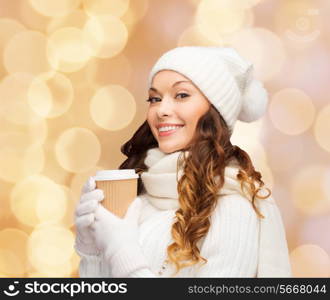 happiness, winter holidays, christmas, beverages and people concept - smiling young woman in white hat and mittens with coffee cup over beige lights background