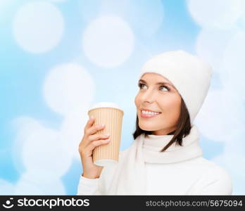 happiness, winter holidays, christmas, beverages and people concept - smiling young woman in white hat and mittens with coffee cup over blue lights background