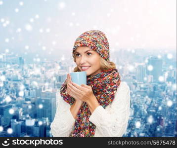 happiness, winter holidays, christmas, beverages and people concept - smiling young woman in warm clothes with cup over snowy city background