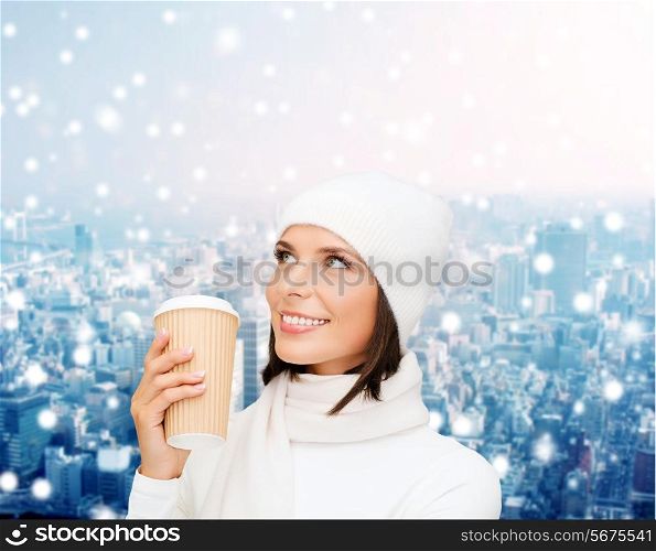 happiness, winter holidays, christmas, beverages and people concept - smiling young woman in white hat and mittens with coffee cup over snowy city background
