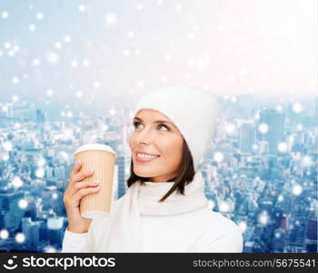 happiness, winter holidays, christmas, beverages and people concept - smiling young woman in white hat and mittens with coffee cup over snowy city background