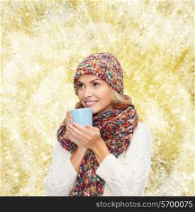 happiness, winter holidays, christmas, beverages and people concept - smiling young woman in warm clothes with cup over yellow lights background