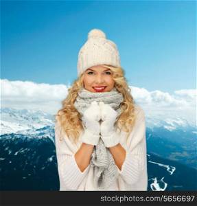 happiness, winter holidays, tourism, travel and people concept - smiling young woman in white hat and mittens over snowy mountains background