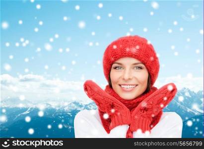 happiness, winter holidays, tourism, travel and people concept - smiling young woman in red hat and mittens over snowy mountains background