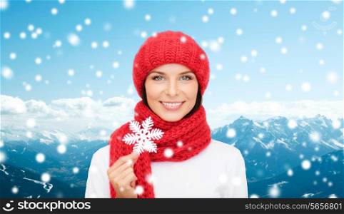 happiness, winter holidays, tourism, travel and people concept - smiling young woman in red hat and mittens holding snowflake over snowy mountains background