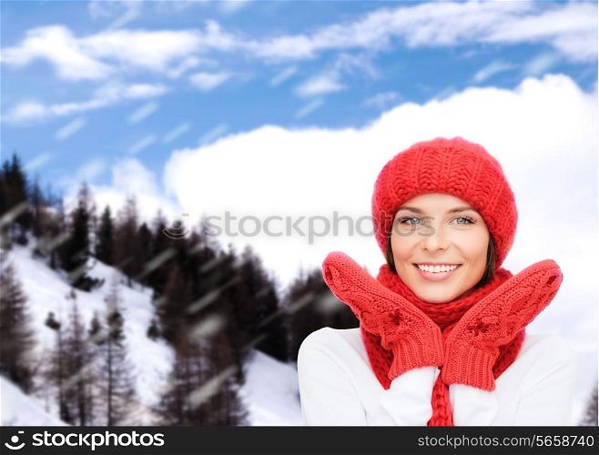 happiness, winter holidays, tourism, travel and people concept - smiling young woman in red hat and mittens over snowy mountains background