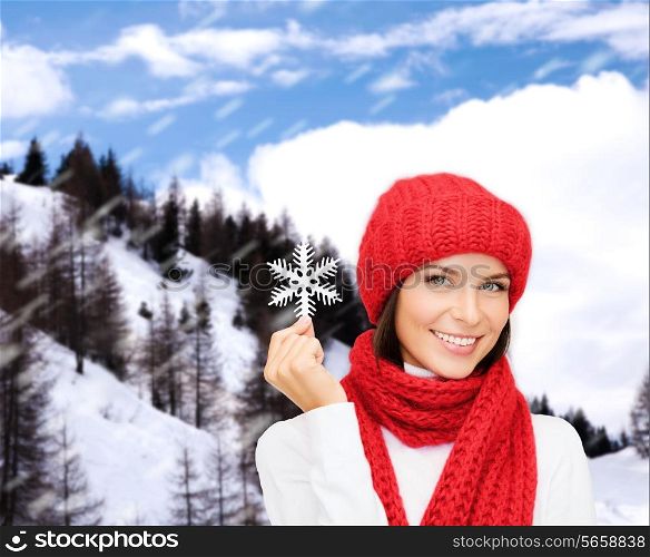happiness, winter holidays, tourism, travel and people concept - smiling young woman in red hat and mittens holding snowflake over snowy mountains background