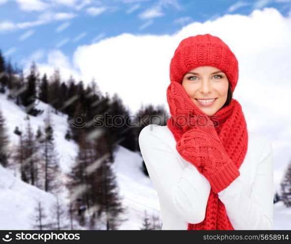 happiness, winter holidays, tourism, travel and people concept - smiling young woman in red hat and mittens over snowy mountains background