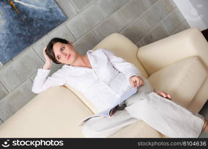 happpy young woman reading magazina at home in comfortabel sofa and bright living room