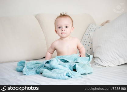Happy 9 months old baby boy sitting on bed after bathing