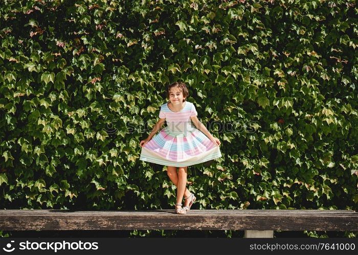 Happy 9-year-old girl in a pretty dress playing in front of a wall of green leaves. Happy 9-year-old girl in a pretty dress playing
