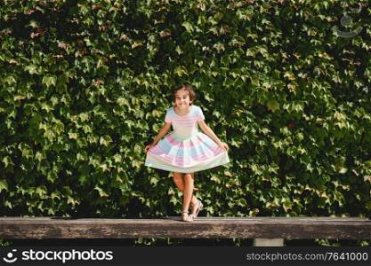 Happy 9-year-old girl in a pretty dress playing in front of a wall of green leaves. Happy 9-year-old girl in a pretty dress playing