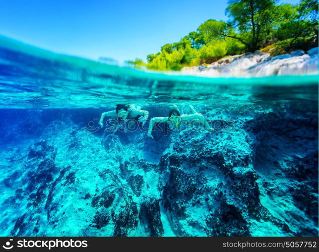 Happy active couple diving near beautiful tropical island, wearing snorkel and mask exploring sea bottom, summer vacation concept