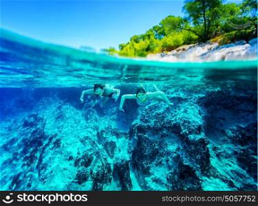 Happy active couple diving near beautiful tropical island, wearing snorkel and mask exploring sea bottom, summer vacation concept