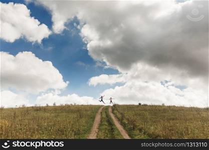 Happy active couple jumping in green field against blue sky with clouds. Summer vacation concept. photo of a couple from afar.. Happy active couple jumping in green field against blue sky with clouds. Summer vacation concept. photo of a couple from afar