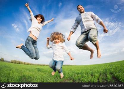 Happy active family jumping in green field against blue sky. Summer vacation concept