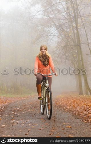 Happy active woman riding bike in autumn park.. Happy active woman riding bike bicycle in foggy fall autumn park. Glad young girl in sweater and earmuffs relaxing. Healthy lifestyle and recreation leisure activity.