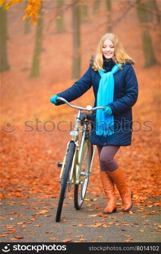 Happy active woman riding bike in autumn park.. Happy active woman riding bike bicycle in fall autumn park. Glad young girl in jacket and scarf relaxing. Healthy lifestyle and recreation leisure activity.