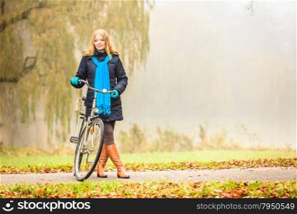 Happy active woman with bike bicycle in foggy fall autumn park. Glad young girl in jacket and scarf relaxing. Healthy lifestyle and recreation leisure activity.