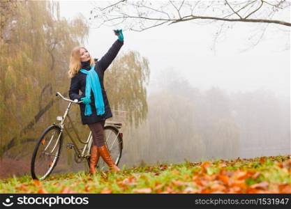 Happy active young woman girl with bike bicycle in fall autumn park taking selfie self photo picture.. Happy woman with bike in park taking selfie photo.
