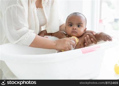 Happy adorable African newborn baby bathing in bathtub. Mother use sponge with shower gel to wash her little daughter in warm water. Newborn baby cleanliness care concept