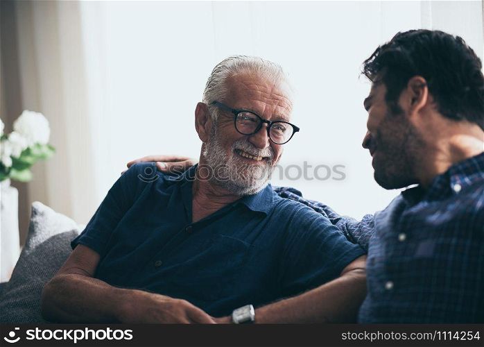 happy adult son and senior father laughing on sofa at home