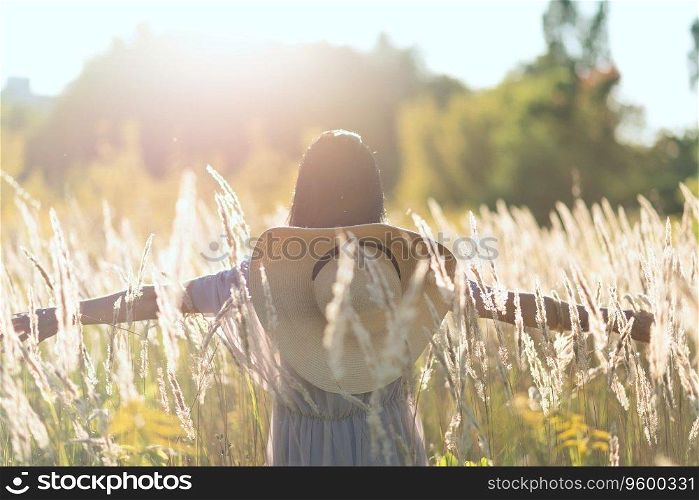 Happy adult woman at summer meadow in a sunset light, chilling outdoor, blurred defocused lifestyle portrait with backlighting haze and plant pollen and dust in air, back view, summer vacation concept. Happy adult woman at summer meadow in sunset light, chilling outdoor, blurred defocused lifestyle portrait with backlighting haze and plant pollen and dust in air, back view, summer vacation concept