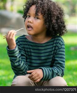 Happy african american child eating snack stick in the park. Children nutrition concept.. Happy african american child eating snack stick.