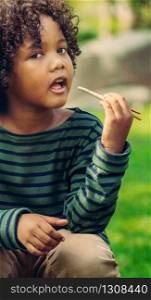 Happy african american child eating snack stick in the park. Children nutrition concept.. Happy african american child eating snack stick.