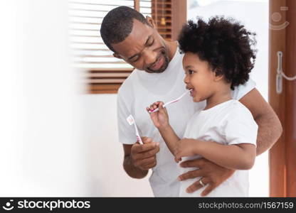 Happy African American Family, Dad teaching his son in white shirts brushing teeth in bathroom together. Father and kid boy in curly hair enjoying with dental hygiene at home in morning